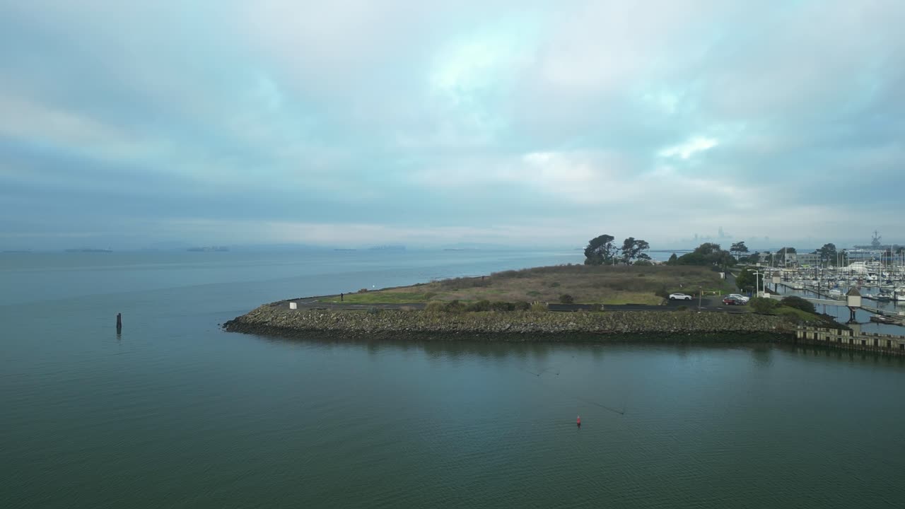 크래브 코브 (crab cove) 의 회전하는 공중 풍경은 푸른 해안선, 반이는 물, 울창한 초록색을 보여줍니다. 알라메다, 캘리포니아, 미국, 구름이 가득한 하늘 아래.