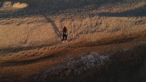 caucasian woman throws rocks from beach seaside into ocean, kafarabida, lebanon, spinning descending aerial