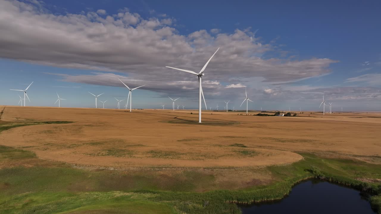 A drone flies up and across a prairie farmland wind farm as windmills spin in southern Alberta, Canada