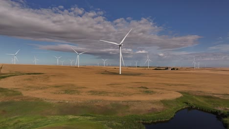 a drone flies up and across a prairie farmland wind farm as windmills spin in southern alberta, canada