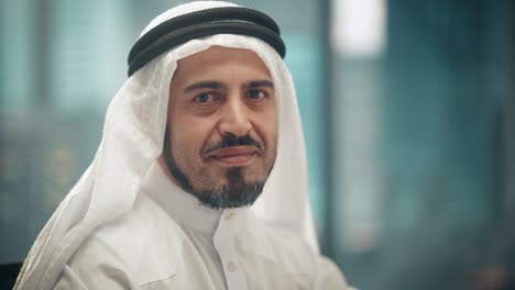 portrait of successful arab businessman in traditional outfit gently smiling, wearing white kandura and black agal keeping a ghutra in place. saudi, emirati, arab businessman concept.