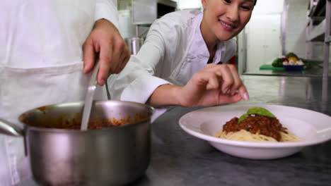 Chef-serving-up-spaghetti-and-another-garnishing-with-basil-leaf