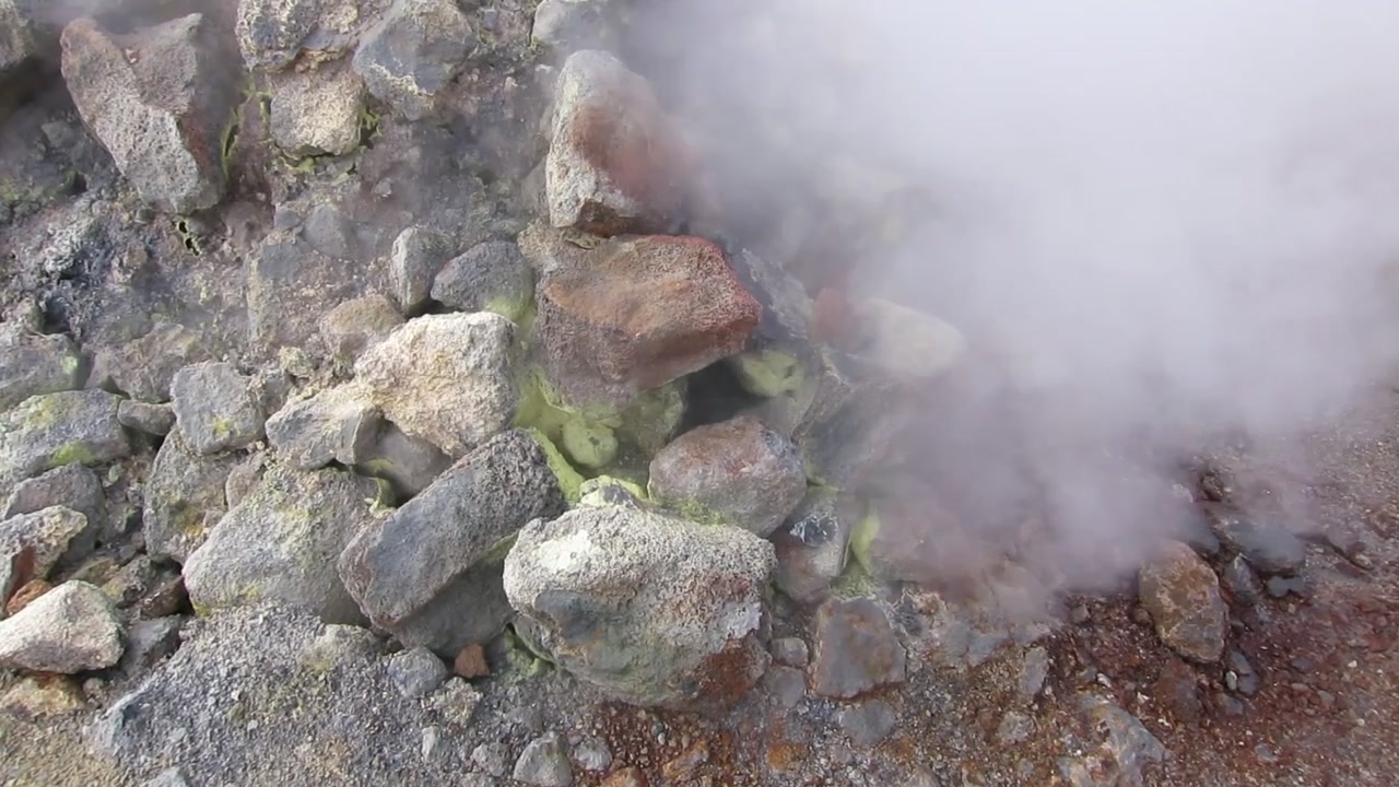 Vista aérea de drone de uma fumarola de enxofre fumegante no campo geotérmico de Namafjall Hverir, perto do Lago Myvatn, no norte da Islândia, com rochas manchadas por minerais, vapor ascendente e solo vulcânico.