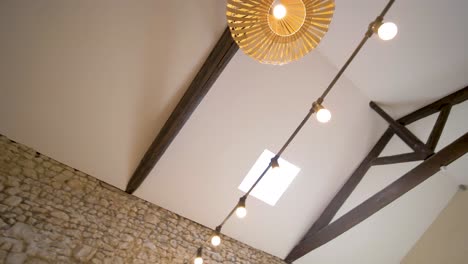 Ceiling-of-modern-country-house-with-rounded-bulbous-wood-lamps-hanging-from-the-beams,-Looking-up-rotating-shot