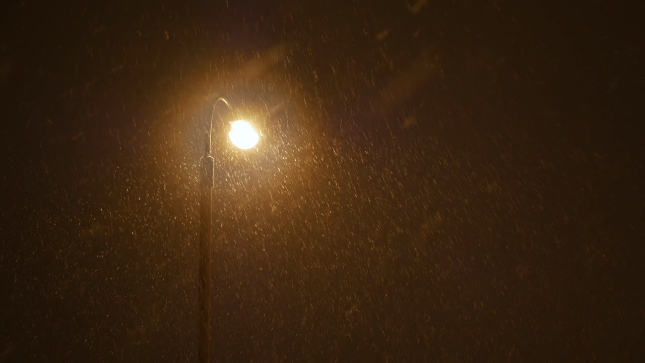 Snow falling in the yellow light of street lamp at night