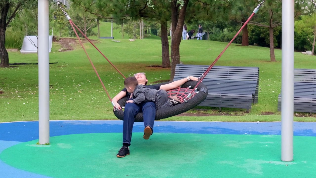 Um menino desfrutando de um grande balanço circular em um parquinho moderno. Ele se deita e depois se senta, balançando suavemente no balanço de rede único.