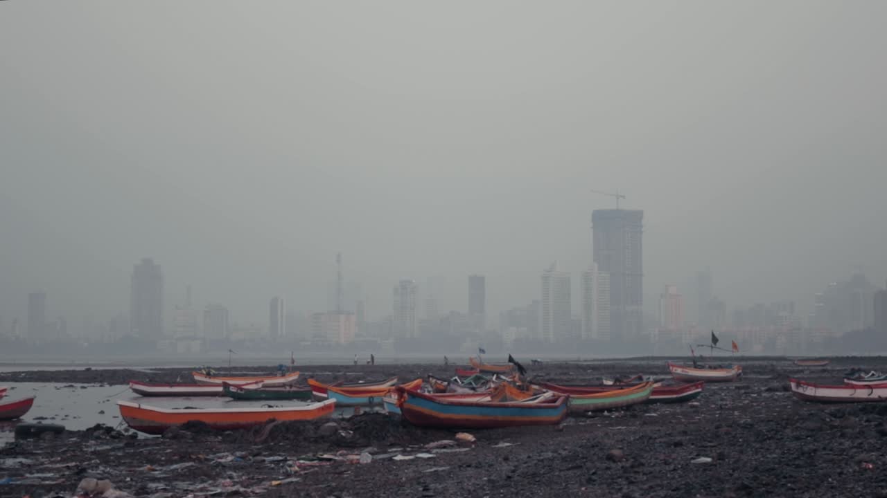 Beached, colourful fishing boats on the Mumbai shore with large buildings in the background