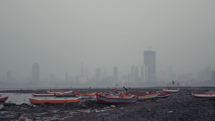 Beached, colourful fishing boats on the Mumbai shore with large buildings in the background