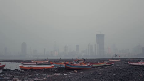 beached, colourful fishing boats on the mumbai shore with large buildings in the background