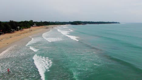 toma aérea, estática, con drones de personas en la playa, mientras las olas golpean una costa paradisíaca, cerca de la ciudad de trincomalee, en un día nublado, en gokanna, en la provincia oriental de sri lanka.