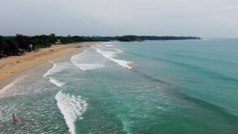 aerial, static, drone shot of people on the beach, while waves hits a paradise coast, near trincomalee city, on a cloudy day, in gokanna, in the eastern province, of sri lanka