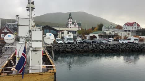 Husavik-Hafen-Hinter-Einem-Traditionellen-Holzboot-Mit-Isländischer-Flagge