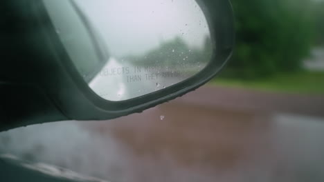 rain drops fall off the passenger side mirror of a car in super slow motion as the car drives