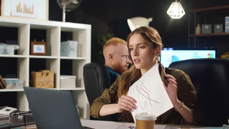 angry business woman arguing about documents during video call in dark office.