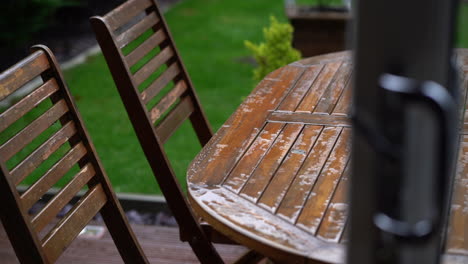lluvia en la mesa de jardín de madera a través de la puerta con sillas de madera y hierba verde mojada