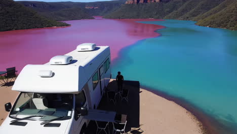 aerial view of campervans by a striking pink and blue lake in nature
