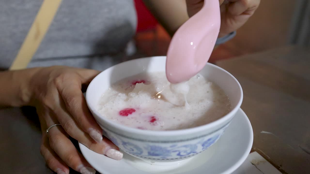 Close-up of woman eating Thai red rubies dessert at night with handheld camera movement