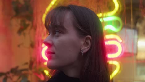 girl looks into camera and turns away in front of bright neon light sign, restaurant venue. woman on a date, blurry lights. cute romantic.