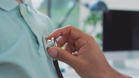 close up of male doctor or gp wearing white coat examining boy listening to chest with stethoscope