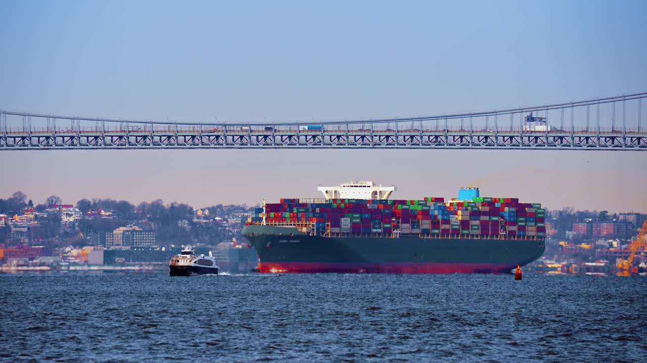 New York, USA, 5 October 2025: Container ship and ferry moving in opposite directions. Large green freighter and small white ferry boat on blue water under long bridge
