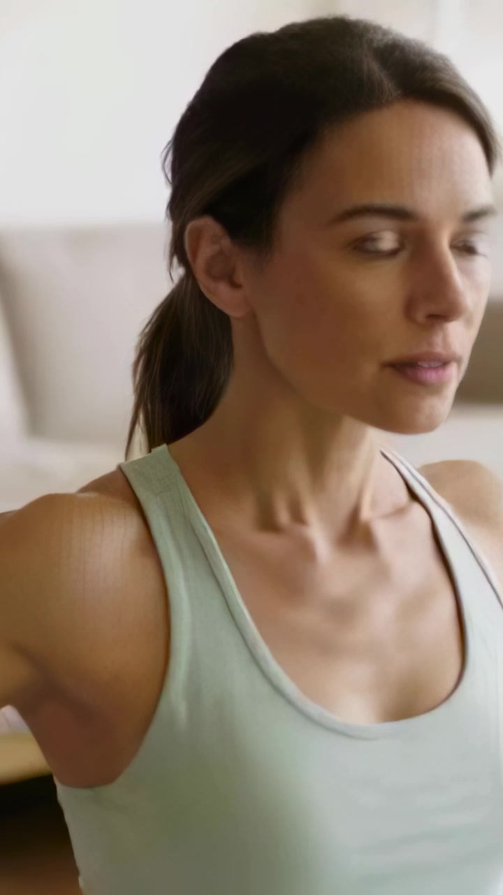 Video verticale: Donna con un top verde che si gira a destra a casa con le braccia alzate per fare stretching.