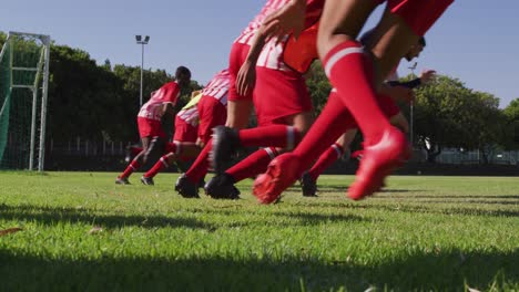 video of diverse group of male football players warming up on field, running