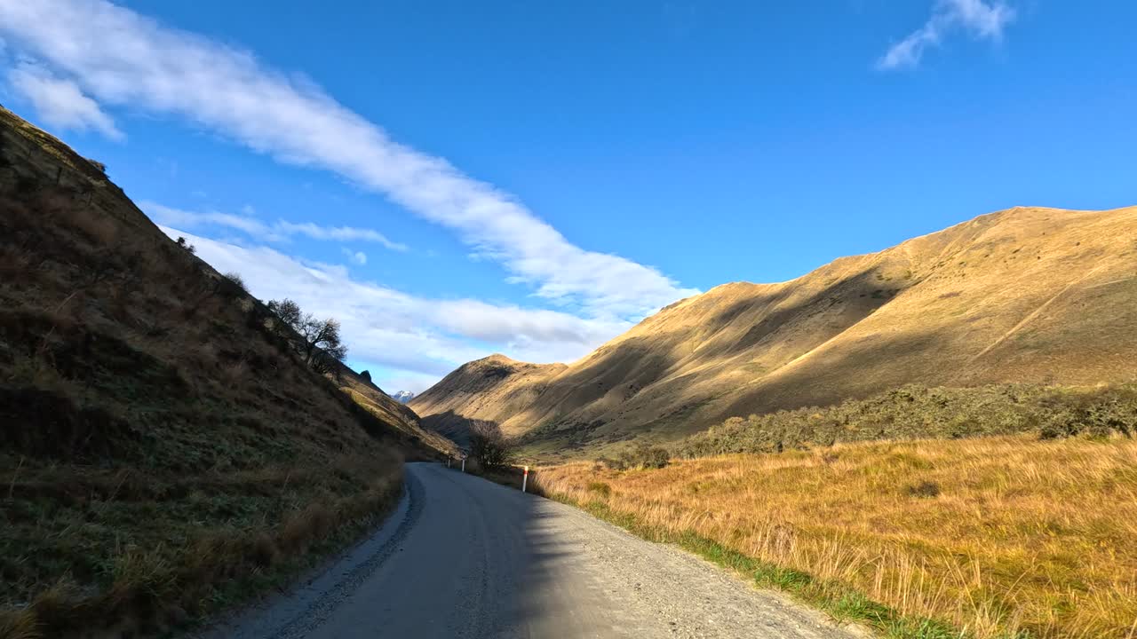 Vehicle travels scenic gravel road through sunlit mountain valley, wide angle, steady camera movement