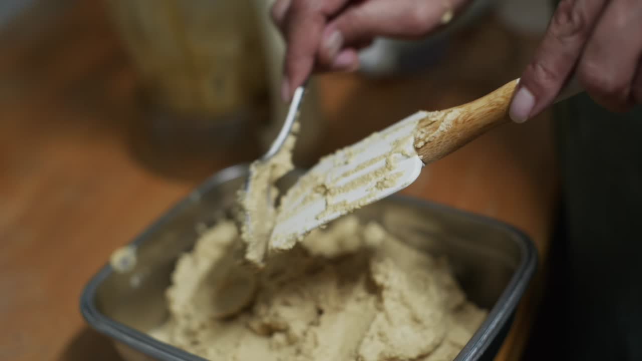pasta de hummus recién hecha raspada de la cuchara de hornear en un recipiente de metal, filmada de cerca en cámara lenta