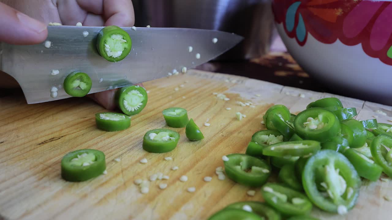 Preparação de alimentos em close-up: picando pimentas jalapeño em uma tábua de corte de madeira.