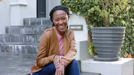 Portrait-of-happy-african-american-woman-sitting-on-steps-in-garden-laughing,-slow-motion