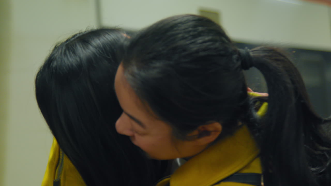 두 명의 젊은 여성 친구들이 지하철 역 플랫폼에서 작별 인사를 하고 안고 있습니다.