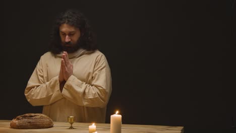 studio shot of man wearing robes with long hair and beard representing figure of jesus christ blessing bread and wine