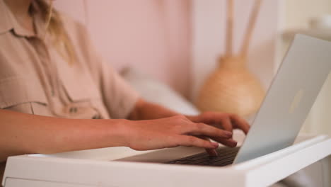 woman types message on keyboard of modern laptop in bed