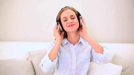 blonde woman listening music and dancing on sofa