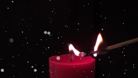 white spots floating against match stick lighting a red candle against black background