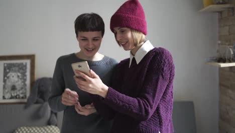 Two-woman-laughing-using-mobile-phone-in-room.-Woman-gossip.-Digital-lifestyle