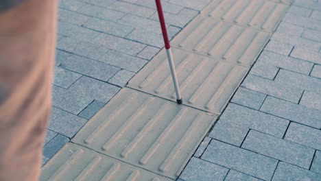 hombre con discapacidad visual está caminando en una baldosa de advertencia táctil con la ayuda de su bastón. superficie de advertencia detectable para los discapacitados visuales al aire libre en la ciudad.