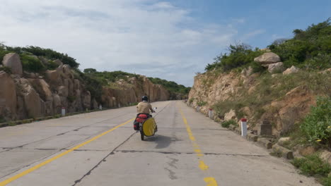 traveler on vacation riding motor bike with surfboard racked on a road