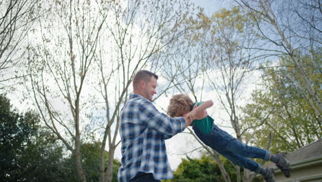 happy father and son playing together in backyard garden happy little boy having fun with dad holding child playfully swinging his kid enjoying childhood freedom outdoors 4k