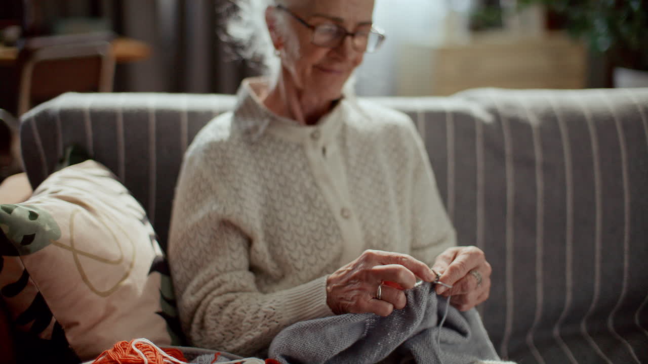 Smiling Elderly Woman Knitting on Sofa at Home
