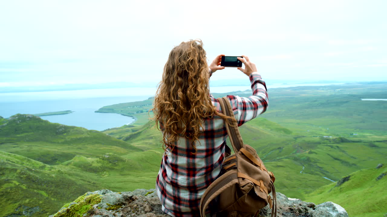 mujer tomando una foto de un paisaje panorámico desde la cima de la montaña