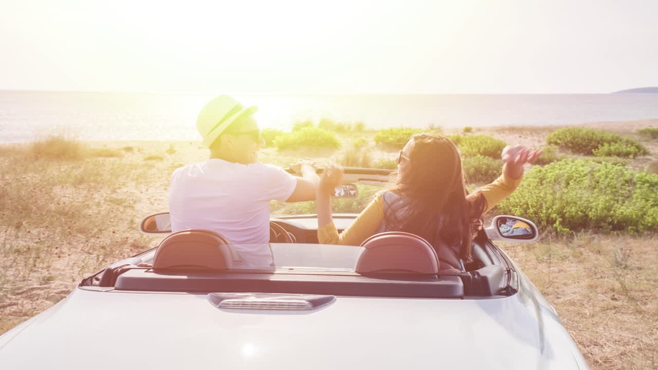 커플이 캐버리블 자동차로 해변 로드 트립을 즐기고 있습니다.