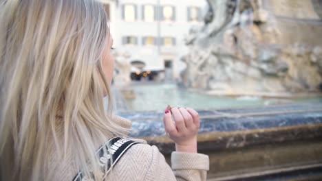 a blonde girl throwing coin in old fountain