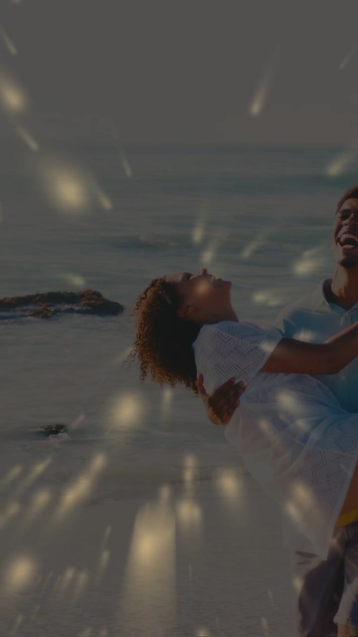Video verticale: Onda leggera che lambisce mentre un uomo solleva e trasporta una donna per divertimento mentre scintille dorate si diffondono.