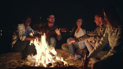 friends singing song by campfire while camping at night