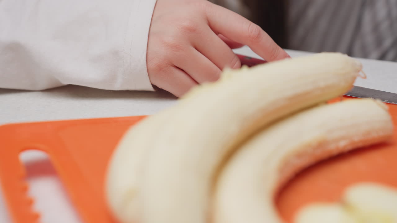 Close up hands peel banana in kitchen, placing fruit with unpeeled bunch while friend reaches to take peel to eat, blue manicure visible, soft blur background, clean counter, lively snack prep moment