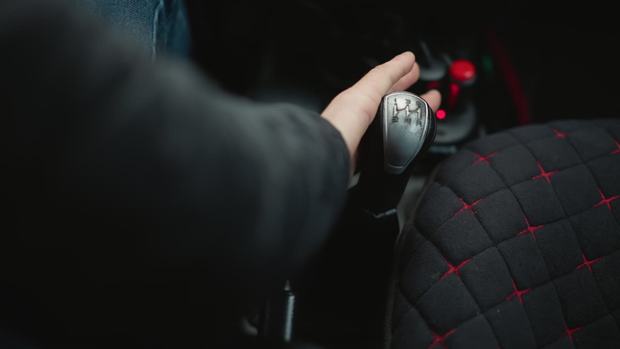 High angle view of urban driver adjusting hand brake lever inside car cabin, quilted seat cover visible, gear knob in frame, showcasing precise tactile control and routine during city commute