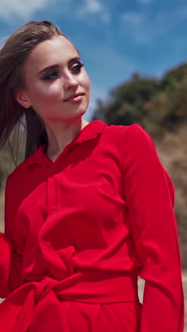 portrait of attractive young woman. gorgeous female in red dress standing among nature in summer with closed eyes. vertical video