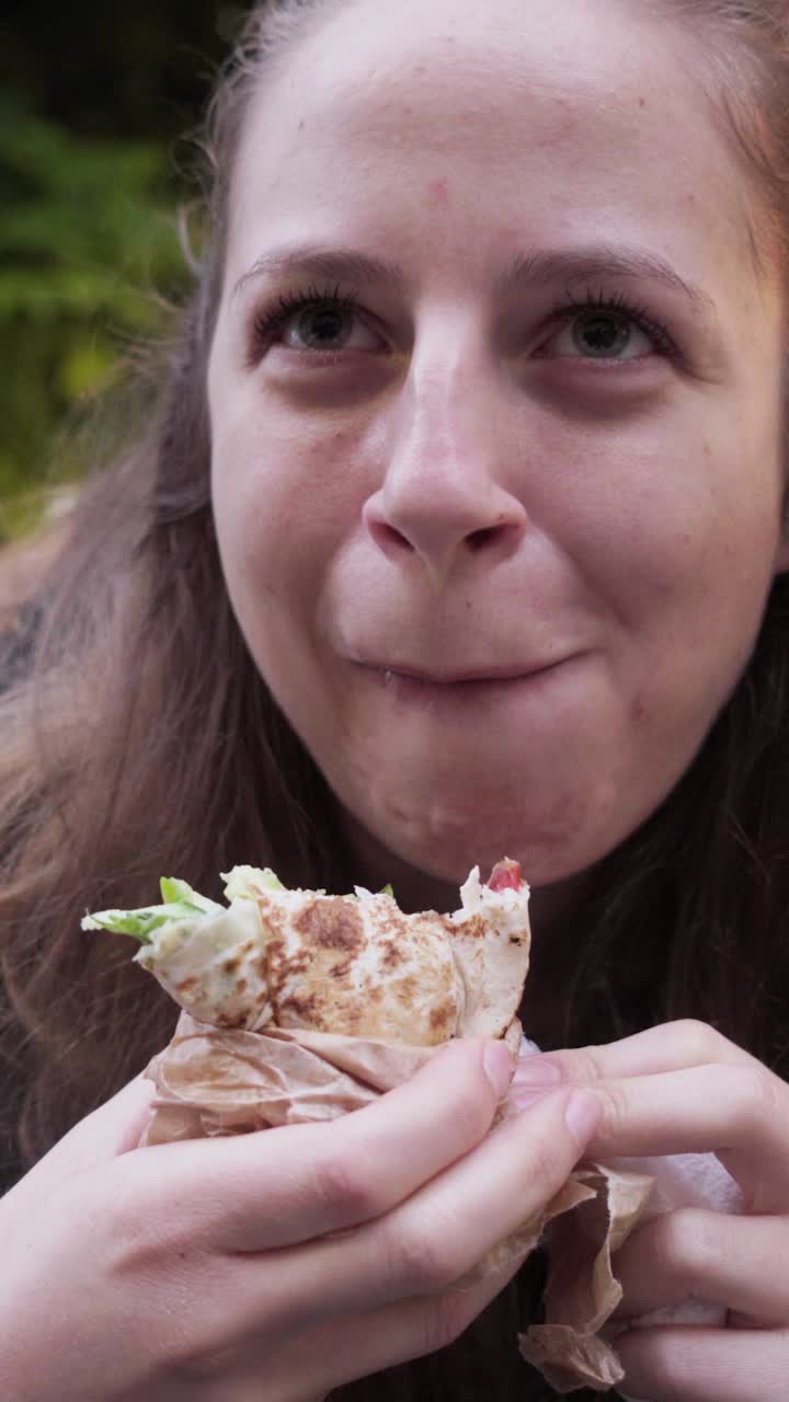 A girl bites into a tasty falafel wrap while standing near a popular food stand in the heart of Sofia