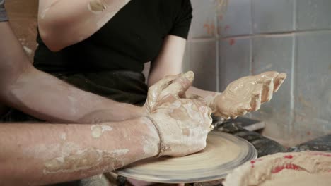 a potter teaches a woman to make clay dishes. a man takes a woman's hands